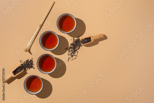 Black puer tea in ceramics bowls,dry pu-erh tea leaves in a wooden bamboo spoons on a beige background,tea ceremony minimalism. photo