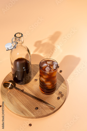 Cold brew coffee in glass on wooden tray,beige background,hard light