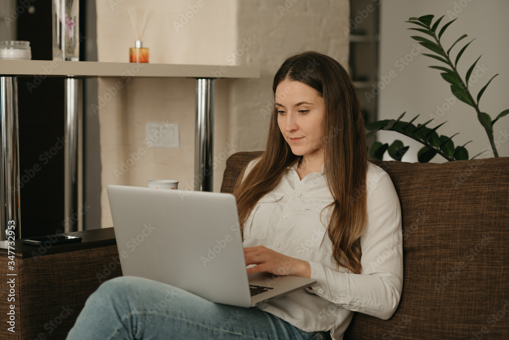 Fototapeta premium Remote work. A caucasian woman working remotely on her laptop. A businesswoman working from home on the sofa.