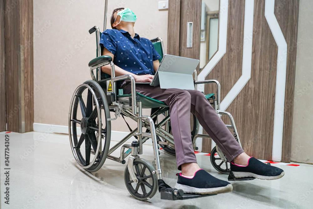 Obraz premium woman wearing medical mask while sitting on wheelchair a hold digital tablet at hospital