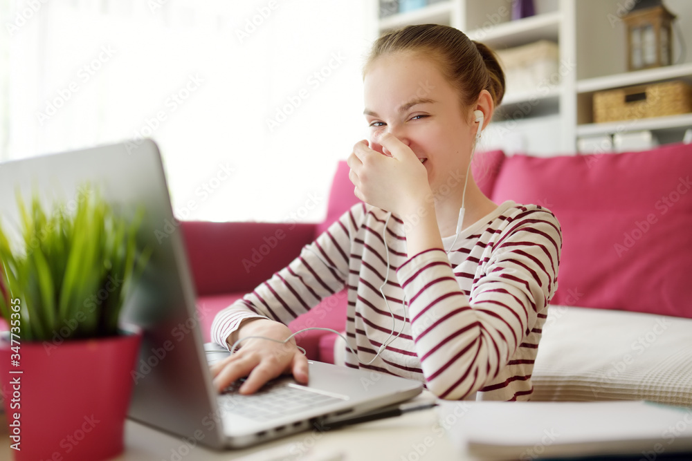 Preteen schoolgirl doing her homework with laptop computer at home ...
