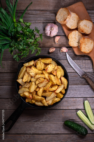 Fried potatoes in a rural style, with spices and fresh greens on rustic pan, on a wooden table. Top view.