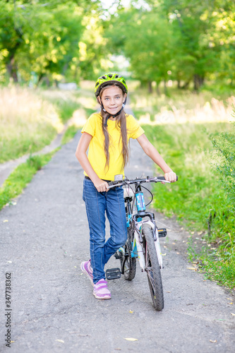 Happy young girl stands with her bike and looks at camera