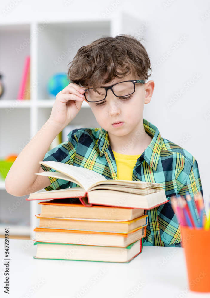 Smart boy wearing eyeglasses doing homework with books Smart boy wearing eyeglasses doing homework with books
