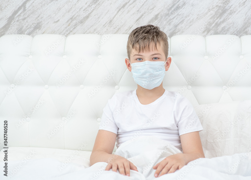 Boy wearing medical protective mask sits on a bed at home. Quarantine and coronavirus epidemic concept. Empty space for text Boy wearing medical protective mask sits on a bed at home. Quarantine and coronavirus epidemic concept. Empty space for text