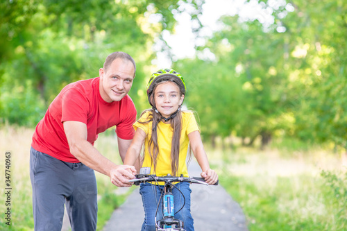 Activity leisure family. Father teaches his daughter to ride a bicycle in the summer park. Empty space for text