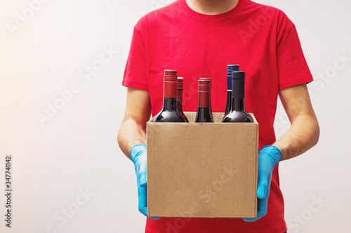 Courier wearing protective gloves holding box with bottles of wine. photo