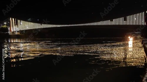 A basket of fire floats under a luminous bridge along the sacred river Ganges in the dark. Hinduism aarti religious ceremony flowers and candles on the sacred river Ganges water in Rishikesh, India photo