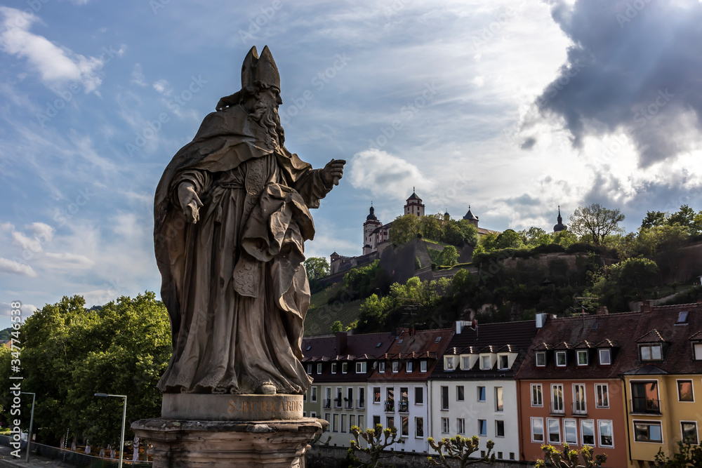 Fototapeta premium Würzburg, Germany - 10th May 2020: A german photographer visiting the city center, taking pictures of religious statues on the footbridge called old Maria bridge at a cloudy day in spring.