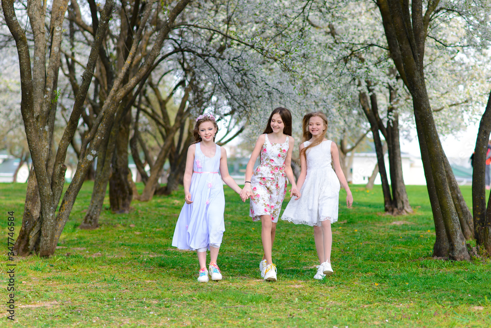 Three adorable girls in dresses hold hands in the garden, park. Three adorable girls in dresses hold hands in the garden, park.