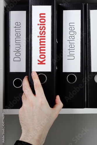 Kommission – Finanzen/Statistik. Ordner im Büro-Regal. Hand greift Unterlagen im Schrank. Beschriftung mit Wort