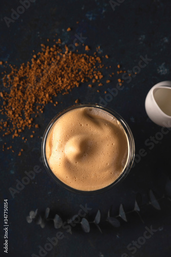 Homemade dalgona coffee made of instant coffee, sugar and milk on a dark background with ice.