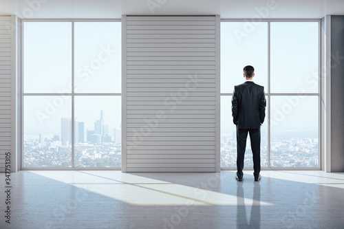 Businessman standing in exhibition interior and looking to city.