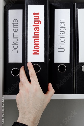 Nominalgut – Finanzen/Statistik. Ordner im Büro-Regal. Hand greift Unterlagen im Schrank. Beschriftung mit Wort photo