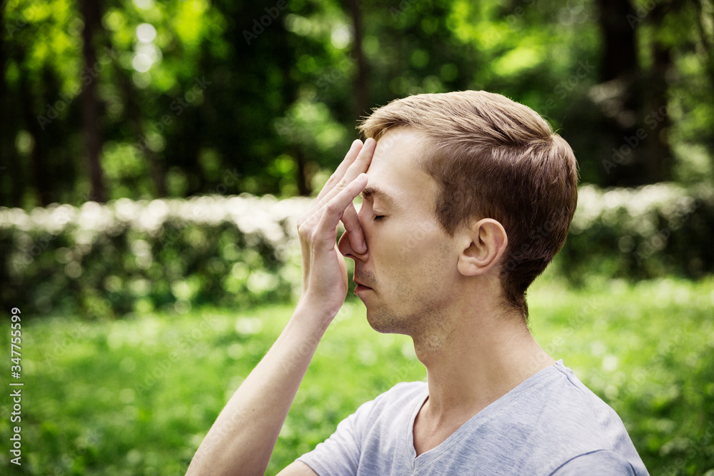Young man doing yoga meditation exercises, symbolic hand gestures mudra. on the background of green forest.