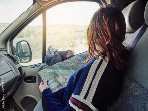 Young girl on her back looking at a map inside a car with her feet outside the window. Local travel concept, adventure. Road trip.
