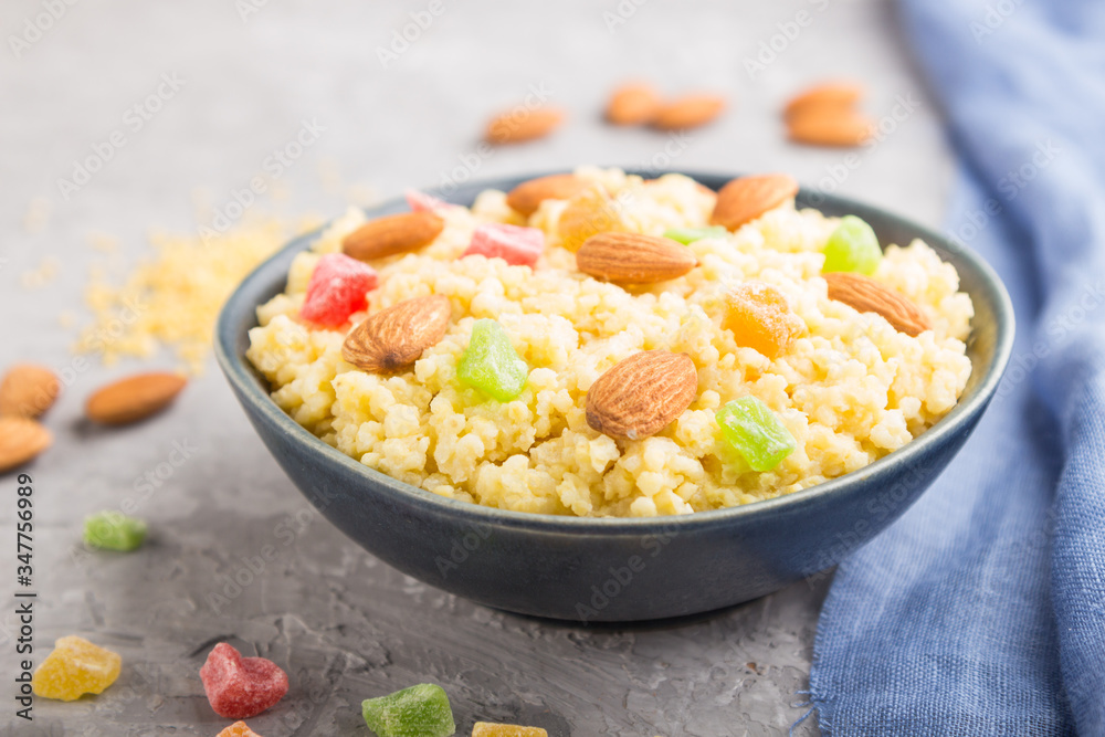 Millet porridge with candied fruits and almonds in blue ceramic bowl on a gray concrete background. Side view, selective focus. Millet porridge with candied fruits and almonds in blue ceramic bowl on a gray concrete background. Side view, selective focus.