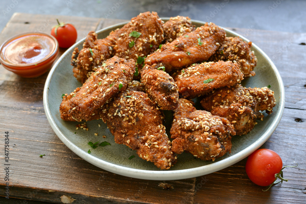 Baked chicken wings with sesame seeds. Ketchup and chili sauce. Free space for text. Wooden background. Delicious fried chicken wings. Close up