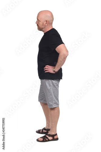 bald man in profile with shirt shorts and sandals, hand on hip