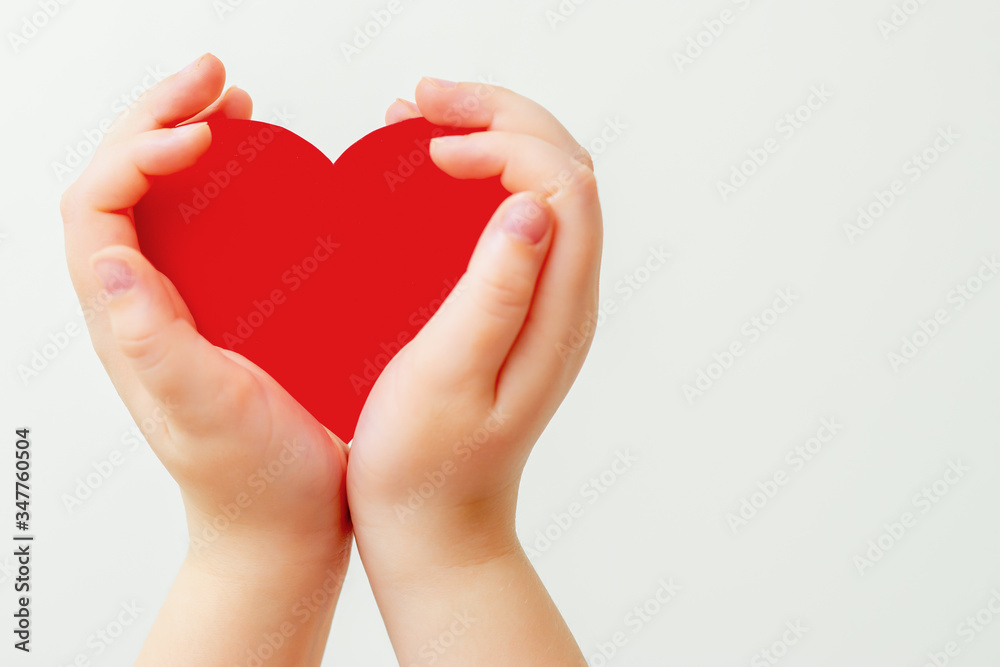 Closeup of child's hands holding paper red heart on white background. Concept of love.