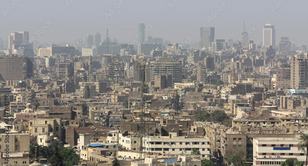 A panoramic view in daylight and sunshine over the big city of Cairo in Egypt. To see with medium-sized buildings and their roofs and in the background many skyscrapers in the haze.