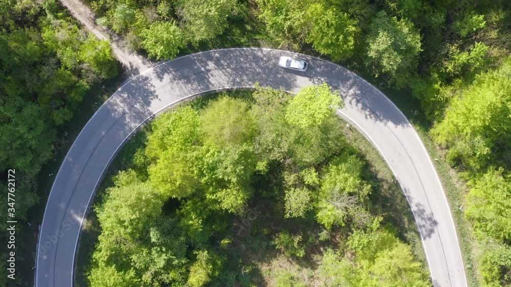 Droneshot of a semicircle curve while two cars are driving though it in a green forest, top shot aerial.
