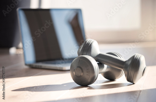 Composing with dumbbells and laptop at home standing for online fitness classes