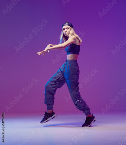 Cute teen girl dancing hip-hop in stylish clothes, a baseball cap, in a Studio with neon lighting. Dance color poster.