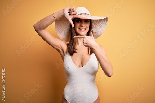 Young beautiful brunette woman on vacation wearing swimsuit and summer hat smiling making frame with hands and fingers with happy face. Creativity and photography concept.