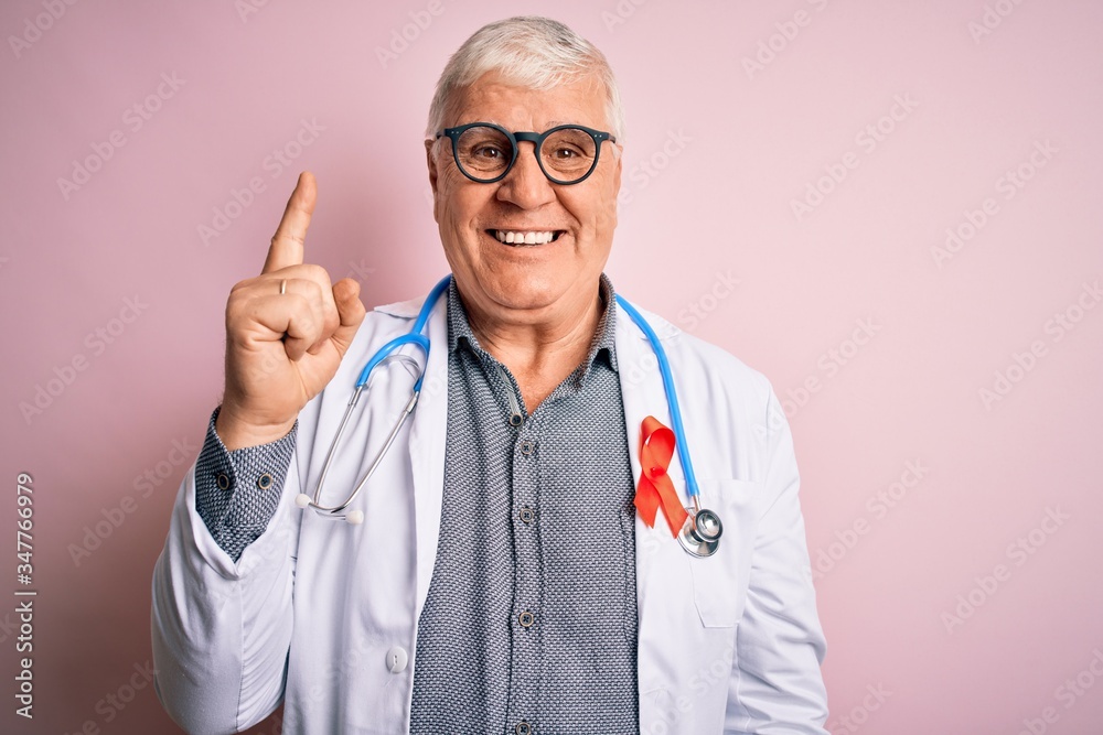 Senior handsome hoary doctor man wearing stethoscope and red HIV ribbon on coat pointing finger up with successful idea. Exited and happy. Number one. Senior handsome hoary doctor man wearing stethoscope and red HIV ribbon on coat pointing finger up with successful idea. Exited and happy. Number one.