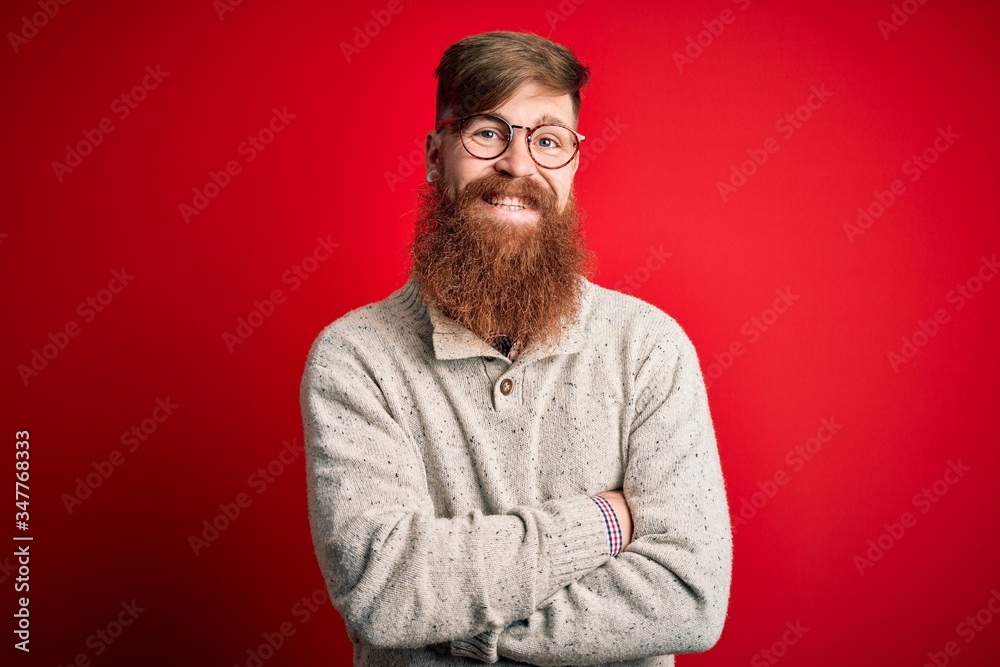Handsome Irish redhead man with beard wearing casual sweater and glasses over red background happy face smiling with crossed arms looking at the camera. Positive person. Handsome Irish redhead man with beard wearing casual sweater and glasses over red background happy face smiling with crossed arms looking at the camera. Positive person.