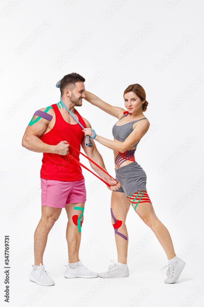 Fototapeta premium Kinesiology taping. Post traumatic rehabilitation, sport physical therapy, recovery concept. Two young male athletes doing exercises with expender.Kinesiology tape on patient knee, shoulder,neck,hip.