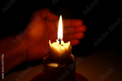 Candle in the dark with a hand covering it from the wind