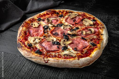 Tasty hot italian pizza with ham, mushrooms and olives on black wooden table. Pizzeria menu. Concept poster for Restaurants or pizzerias