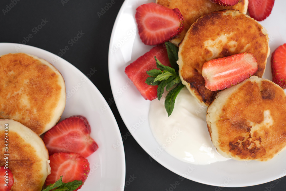 Russian and Ukrainian cuisine. Breakfast. Cottage cheese pancakes. Cheesecakes with fresh strawberries, mint and sour cream sauce in a white plate on a light grey background. close-up top view