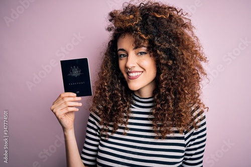Beautiful tourist woman with curly hair and piercing holding australia australian passport id with a happy face standing and smiling with a confident smile showing teeth