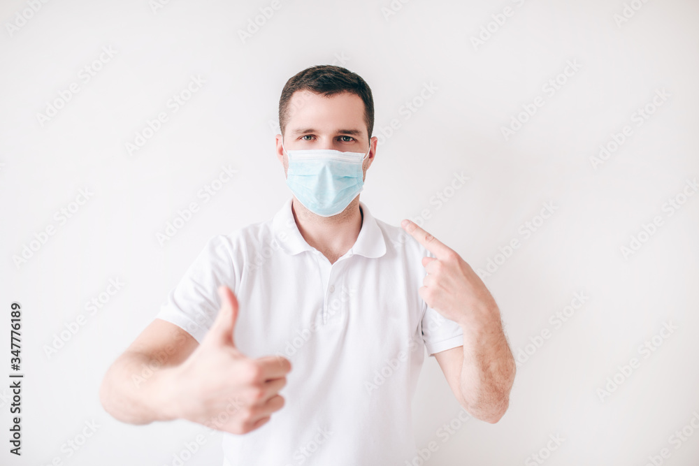 Young sick man isolated over white background. Guy wear facial medical mask for protection. Hold big thumb up. Protect himself from cold and virus. Young sick man isolated over white background. Guy wear facial medical mask for protection. Hold big thumb up. Protect himself from cold and virus.