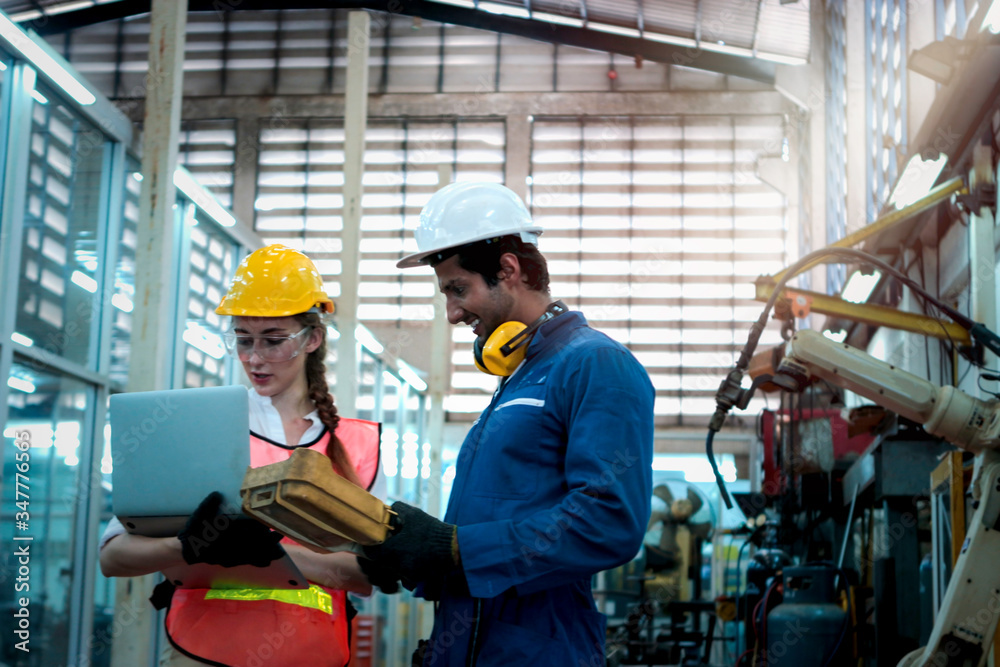Industrial engineer worker woman and man wearing helmet discussing and working together with robot arm for arduino mechanism at manufacturing plant factory, young people working in industry Industrial engineer worker woman and man wearing helmet discussing and working together with robot arm for arduino mechanism at manufacturing plant factory, young people working in industry