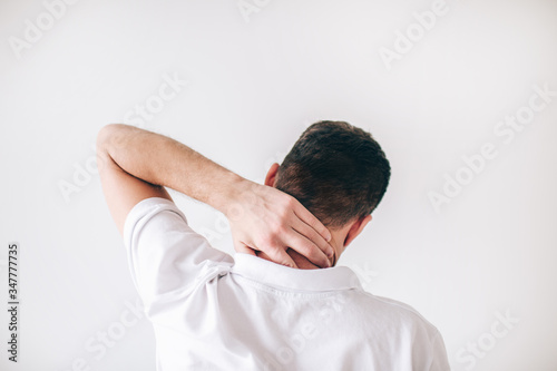 Young man isolated over white background. Back view of guy having troubles with neck. Painful and aching. Man hold hand on back of his neck. © Vlad