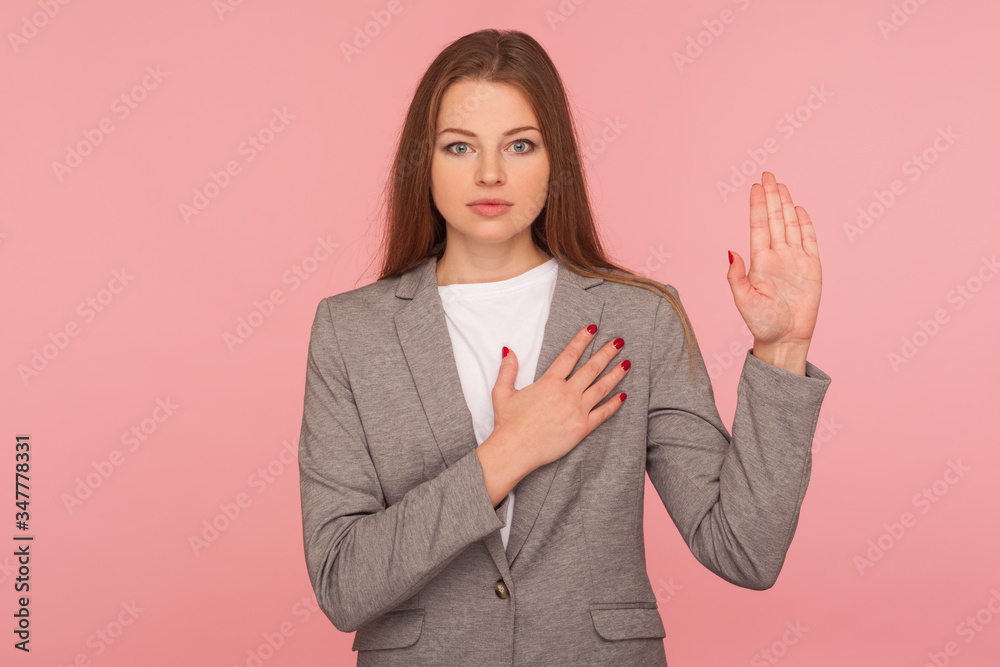 I swear! Portrait of responsible serious young woman in business suit raising hand to take oath, promising to be honest, telling truth, pledging allegiance. studio shot isolated on pink background I swear! Portrait of responsible serious young woman in business suit raising hand to take oath, promising to be honest, telling truth, pledging allegiance. studio shot isolated on pink background