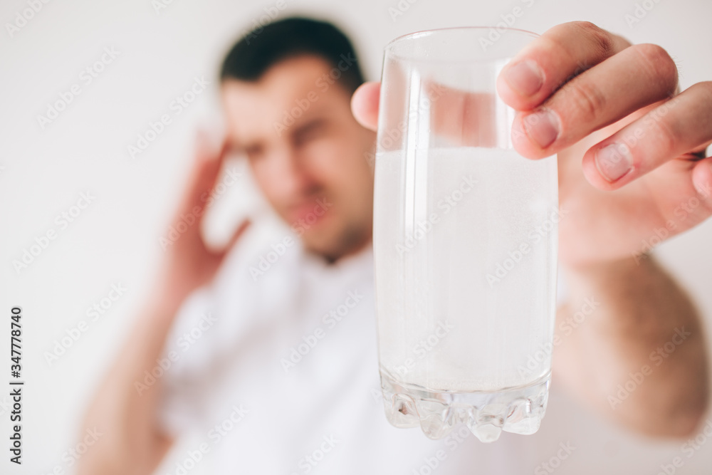 Young sick man isolated over background. Guy hold glass of water with effervescent pills and medicine in it. Suffer from headache and pain. Blurred background. Young sick man isolated over background. Guy hold glass of water with effervescent pills and medicine in it. Suffer from headache and pain. Blurred background.