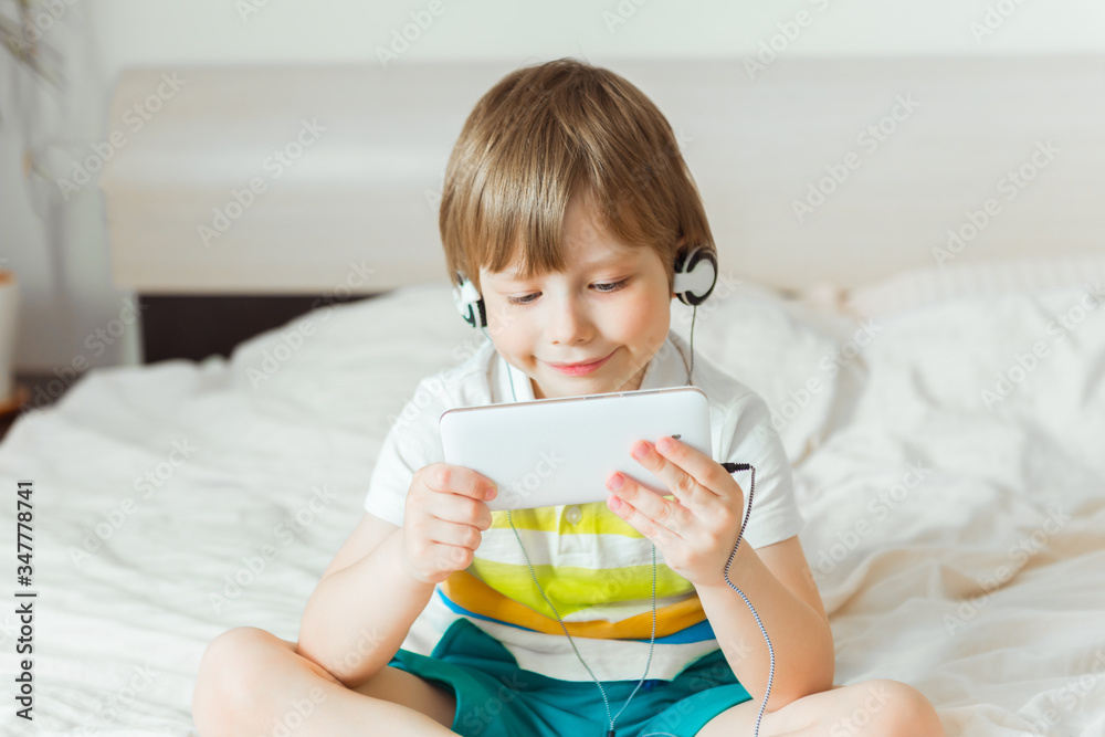 Modern little child sitting on bed with smartphone in his hands Modern little child sitting on bed with smartphone in his hands