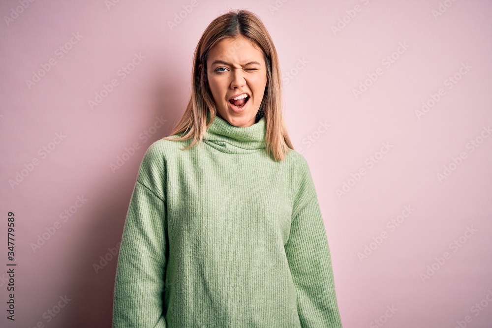 Young beautiful blonde woman wearing winter wool sweater over pink isolated background winking looking at the camera with sexy expression, cheerful and happy face. Young beautiful blonde woman wearing winter wool sweater over pink isolated background winking looking at the camera with sexy expression, cheerful and happy face.