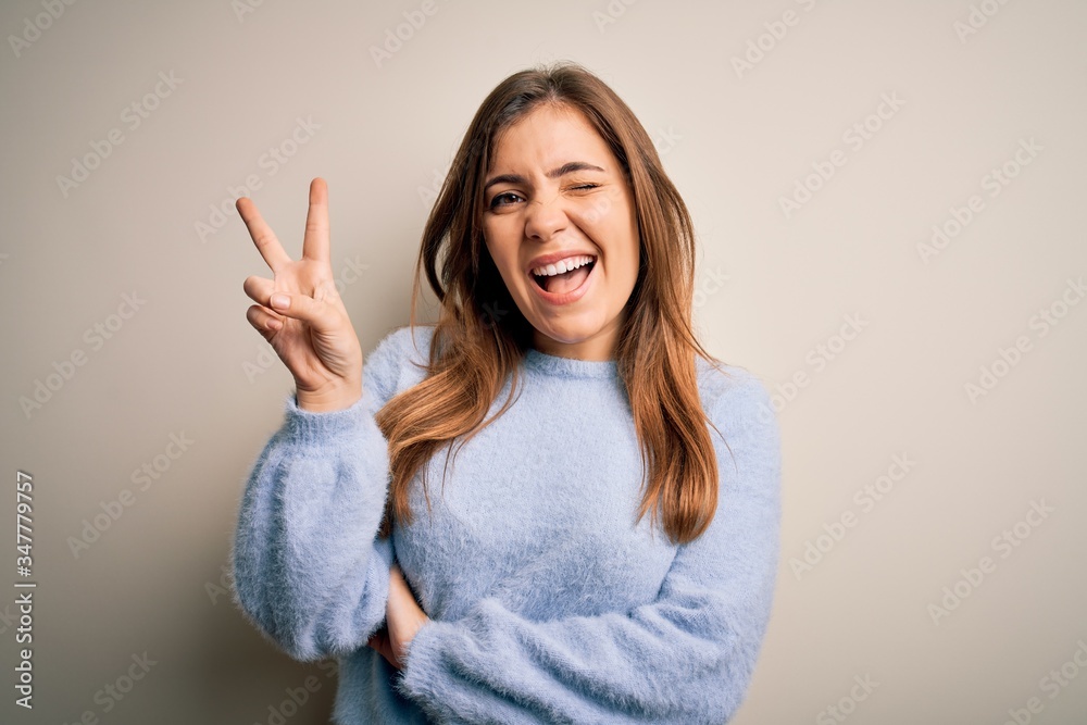 Beautiful young woman wearing casual winter sweater standing over isolated background smiling with happy face winking at the camera doing victory sign. Number two. Beautiful young woman wearing casual winter sweater standing over isolated background smiling with happy face winking at the camera doing victory sign. Number two.