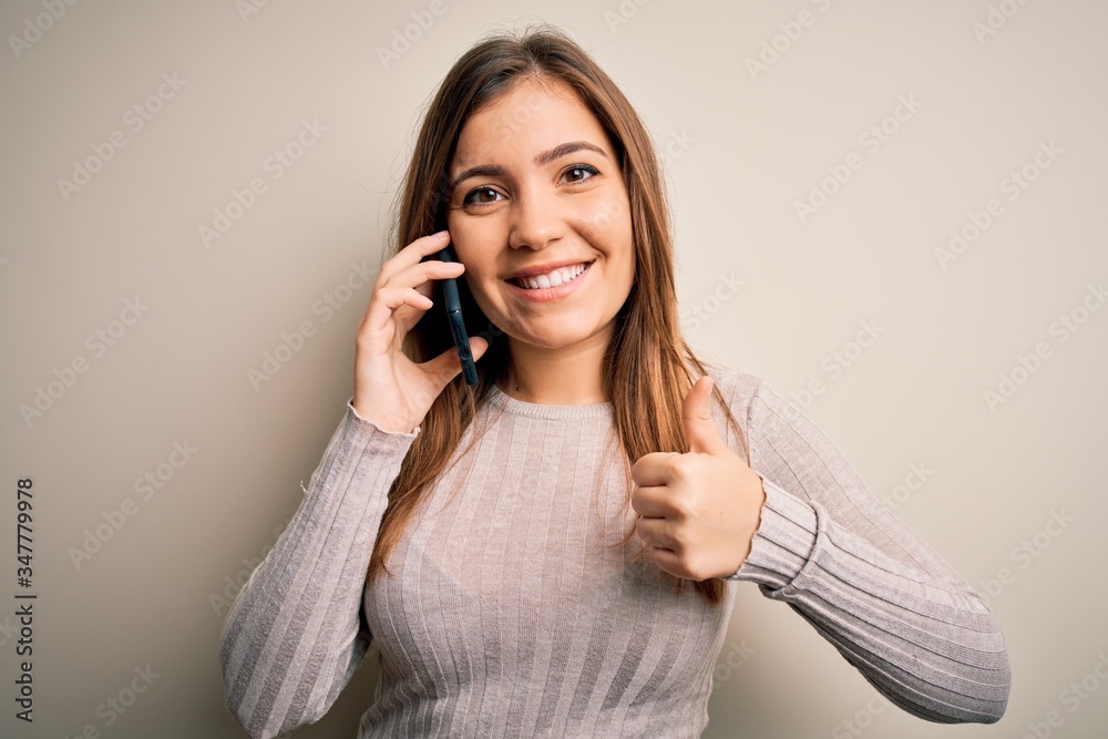 Young woman having a conversation speaking on smartphone over isolated background happy with big smile doing ok sign, thumb up with fingers, excellent sign Young woman having a conversation speaking on smartphone over isolated background happy with big smile doing ok sign, thumb up with fingers, excellent sign