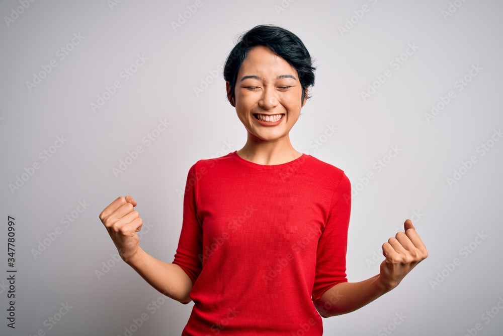 Young beautiful asian girl wearing casual red t-shirt standing over isolated white background very happy and excited doing winner gesture with arms raised, smiling and screaming for success. Celebrate Young beautiful asian girl wearing casual red t-shirt standing over isolated white background very happy and excited doing winner gesture with arms raised, smiling and screaming for success. Celebrate