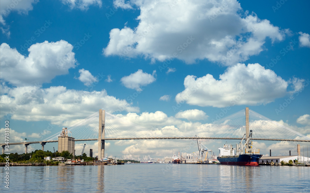 Freight industry at busy harbor on the Savannah River with suspension bridge Freight industry at busy harbor on the Savannah River with suspension bridge