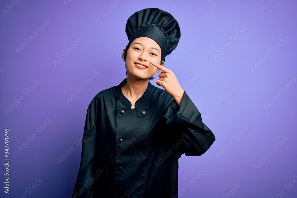 Young beautiful chinese chef woman wearing cooker uniform and hat over purple background Pointing with hand finger to face and nose, smiling cheerful. Beauty concept Young beautiful chinese chef woman wearing cooker uniform and hat over purple background Pointing with hand finger to face and nose, smiling cheerful. Beauty concept
