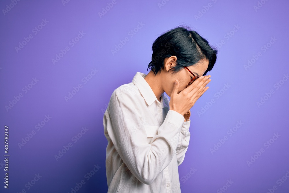 Young beautiful asian girl wearing casual shirt and glasses standing over purple background with sad expression covering face with hands while crying. Depression concept. Young beautiful asian girl wearing casual shirt and glasses standing over purple background with sad expression covering face with hands while crying. Depression concept.