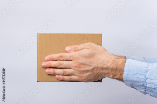 Square cardboard box in male hands. Delivery of parcels. Side view.